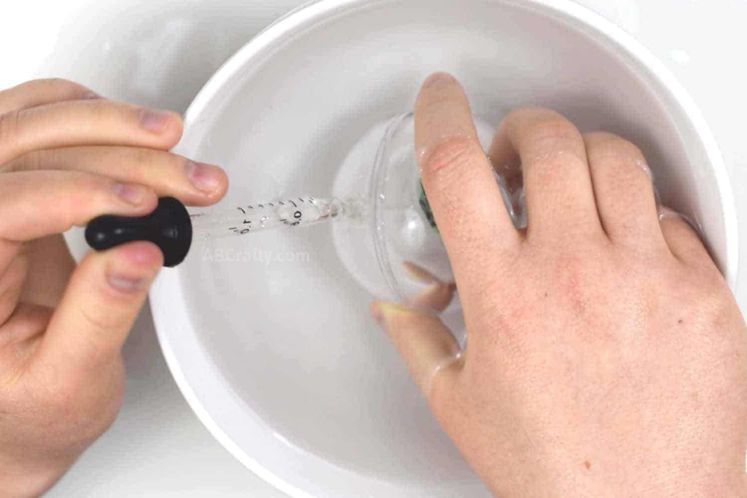 Submerging sealed ornament in a bowl of water and using an eyedropper to remove air and fill it with water
