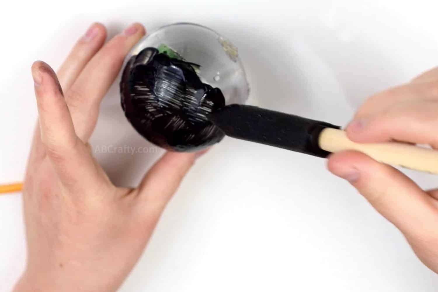 Painting the ornament filled with water with black fabric paint, using a black sponge brush so that it's completely covered like a real magic 8 ball