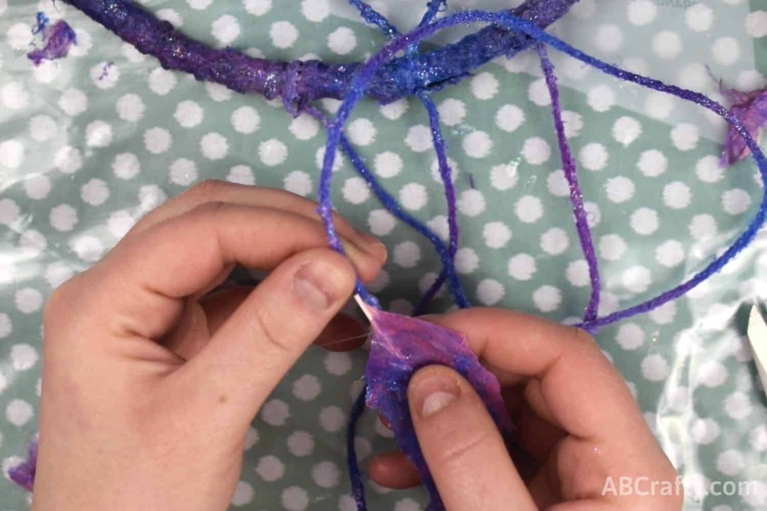 Attaching galaxy painted feather to string of the dream catcher with glue gun