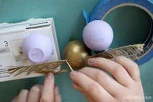 using a toothpick to attach the wings of the Harry Potter golden snitch, which is an eos lip balm with feathers all painted gold