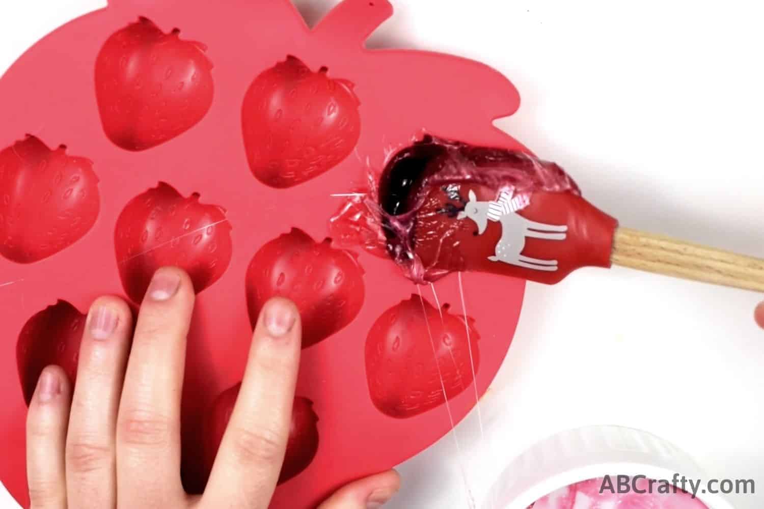 filling the top of the strawberry silicone mold with melted gummy candy with a spatula