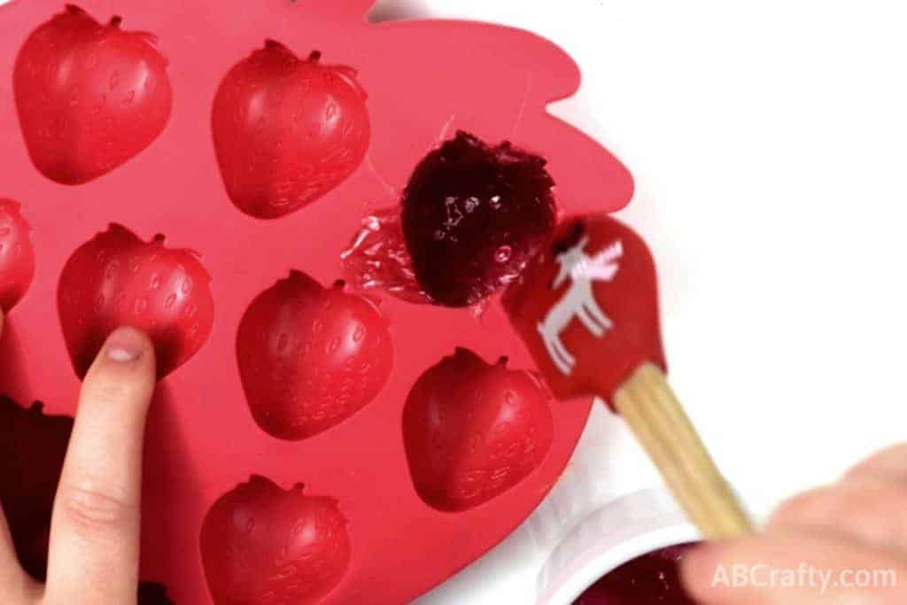 Using a spatula to put melted gummy mixture into a strawberry candy mold