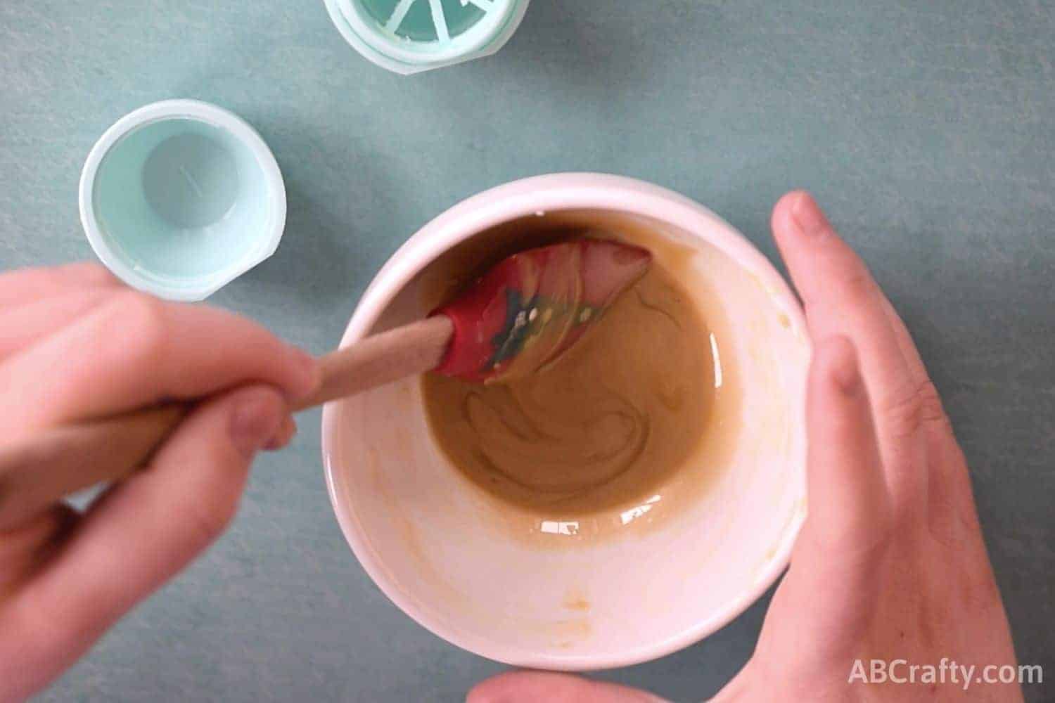 Using a spatula to mix melted golden lip balm ingredients to make the base of a golden snitch harry potter craft