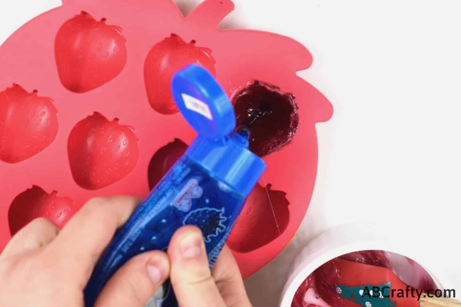 squeezing blue liquid candy into strawberry candy mold with melted gummy fruit candy