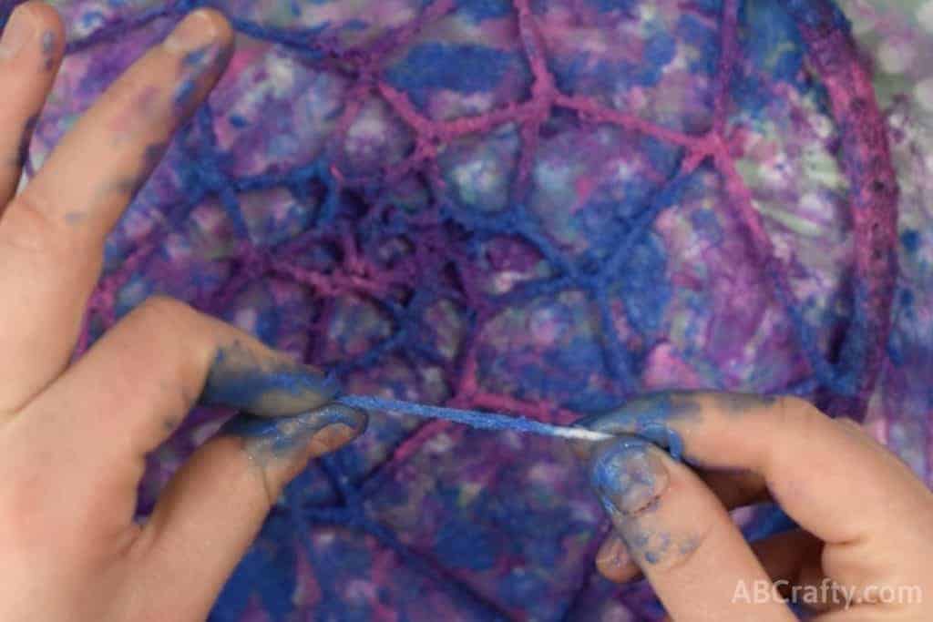 Using fingers to apply fabric paint onto yarn in galaxy colors to the dream catcher