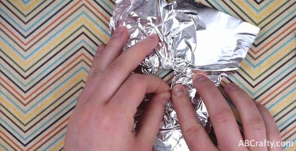 using fingers to push tin foil to make a wall around the hole