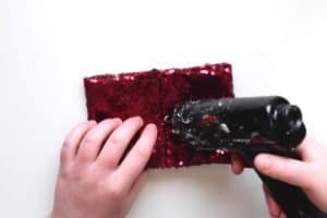 Using a glue gun to add glue to the middle of a rectangle of red sequin fabric