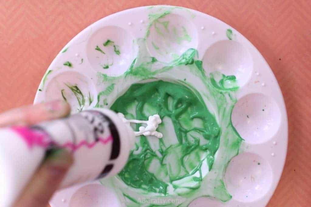 Squeezing white fabric paint to slime green fabric paint on a mixing palette