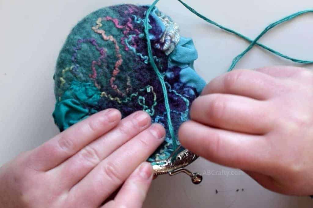 Using teal embroidery thread to sew on silver change purse clasp onto handmade wet felted purse