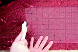 Using a rotary cutter to cut red sequin fabric using a ruler