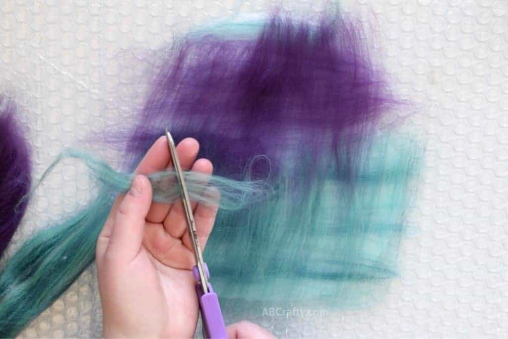 Using scissors to cut teal wool fiber