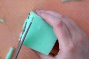 Cutting green foam into the shape of a cube with scissors