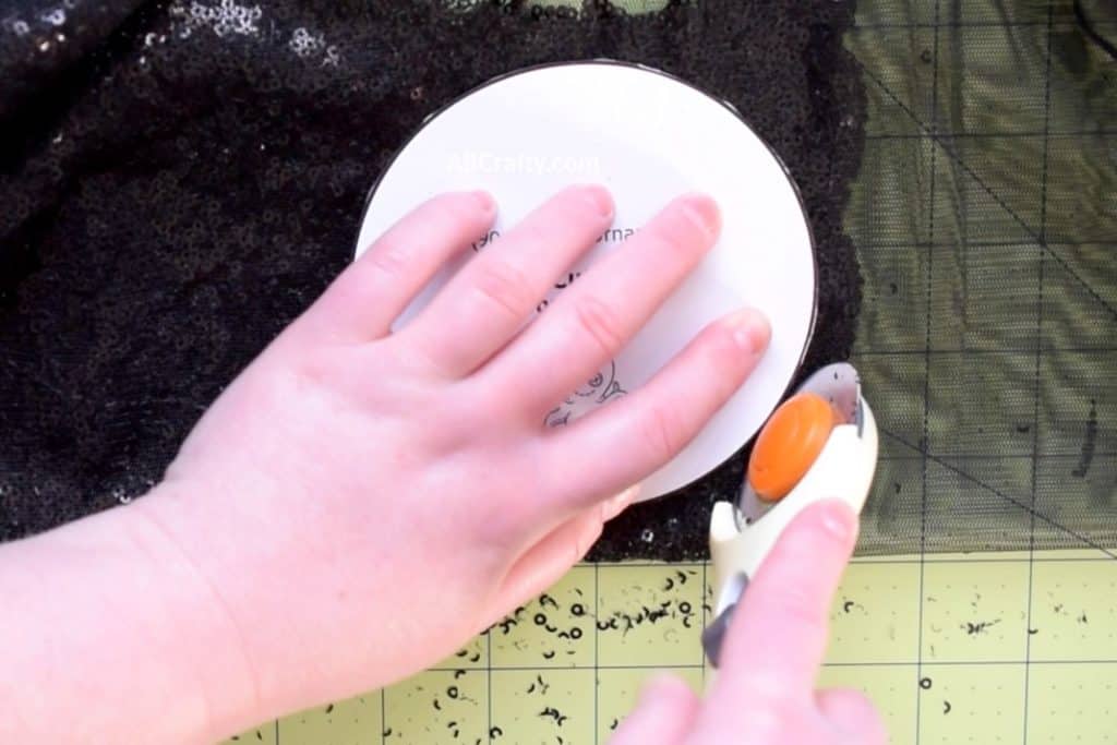 Using a rotary cutter to cut along a printable minnie mouse ears template on black sequin fabric