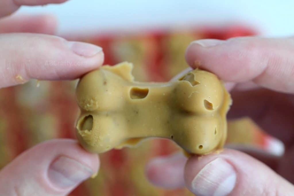 Hands holding a finished homemade peanut butter dog treat that's in the shape of a dog bone