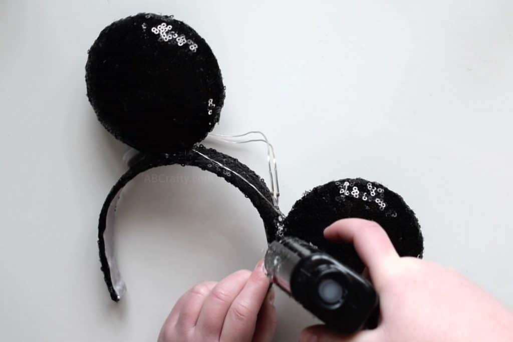 Using a glue gun to glue black sequin circles onto a black sequin headband to create handmade Mickey Mouse ears