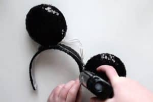 Using a glue gun to glue black sequin circles onto a black sequin headband to create handmade Mickey Mouse ears