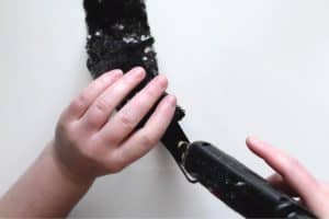 Using a glue gun to glue black sequin fabric onto the sides of a black satin headband