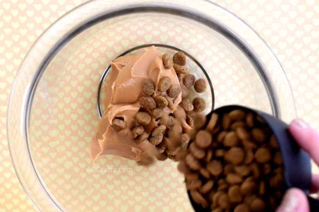 Pouring dry dog food out of a measuring cup into a bowl with peanut butter