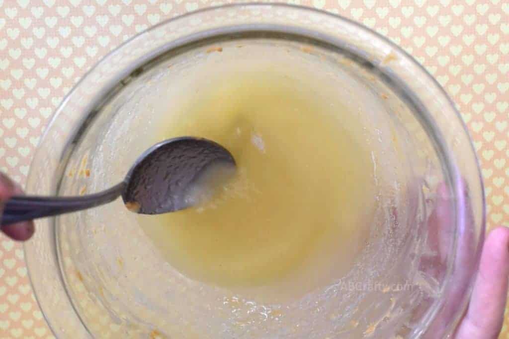 Mixing applesauce and chicken broth with a spoon in a bowl that still has peanut butter stuck to it