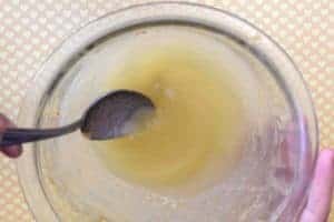 Mixing applesauce and chicken broth with a spoon in a bowl that still has peanut butter stuck to it