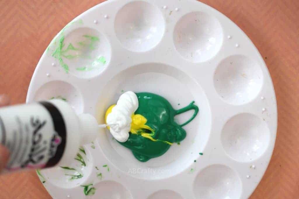 Squeezing white fabric paint into a mixing palette with green and yellow fabric paint