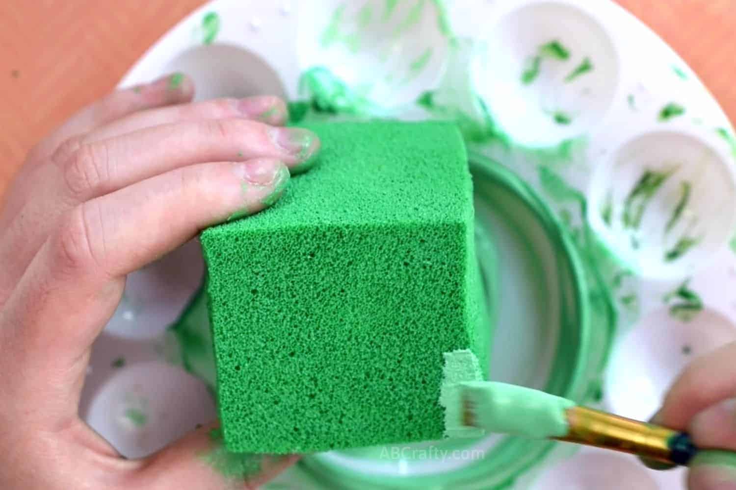Using a paintbrush to paint light green fabric paint onto the edge of a green-painted foam block