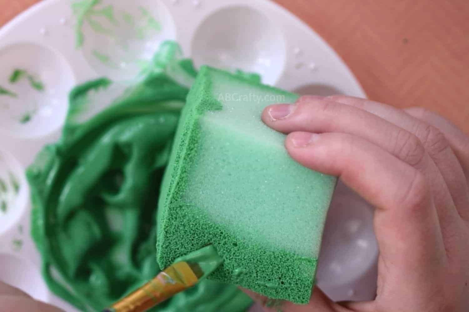 Painting green foam cube with slime-colored fabric paint, using a paint brush
