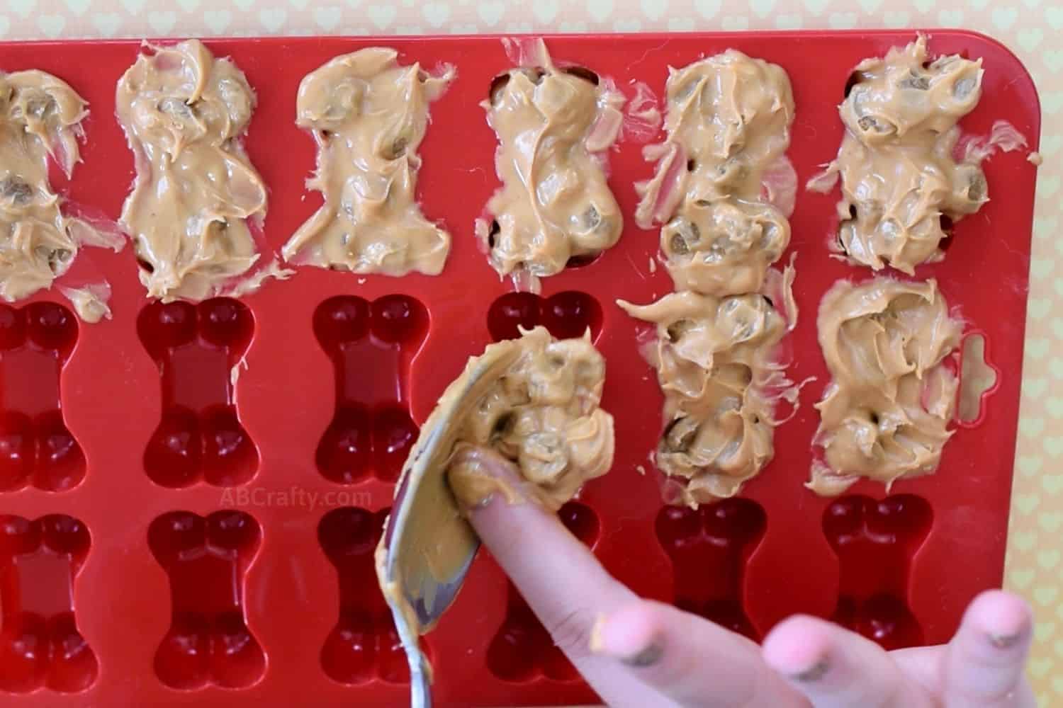Using finger to scrape the peanut butter and dog food kibble mixture into the dog bone silicone mold