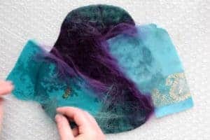 Placing teal and purple merino wool along the edges of scraps of blue and teal sari silk fabric to help it felt to the fiber below