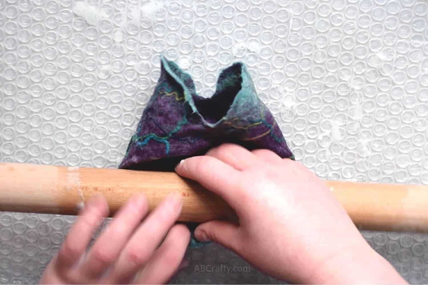 Rolling wet felted pouch on its side with a wooden dowel