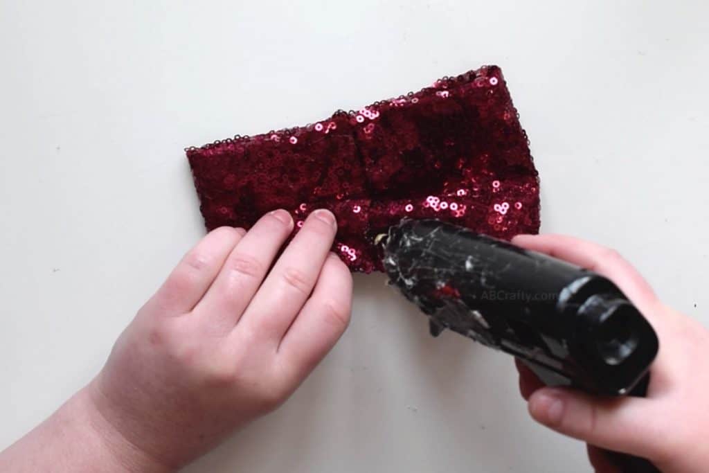 Adding glue to red sequin fabric, shaping folds to a bow