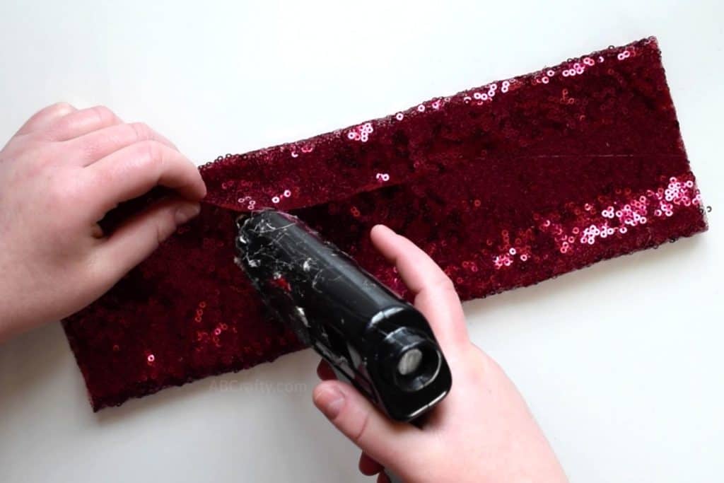 Using a glue gun to glue a rectangle of red sequin fabric in half