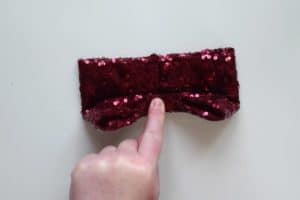 Finger holding the center of half of a bow made of red sequin fabric