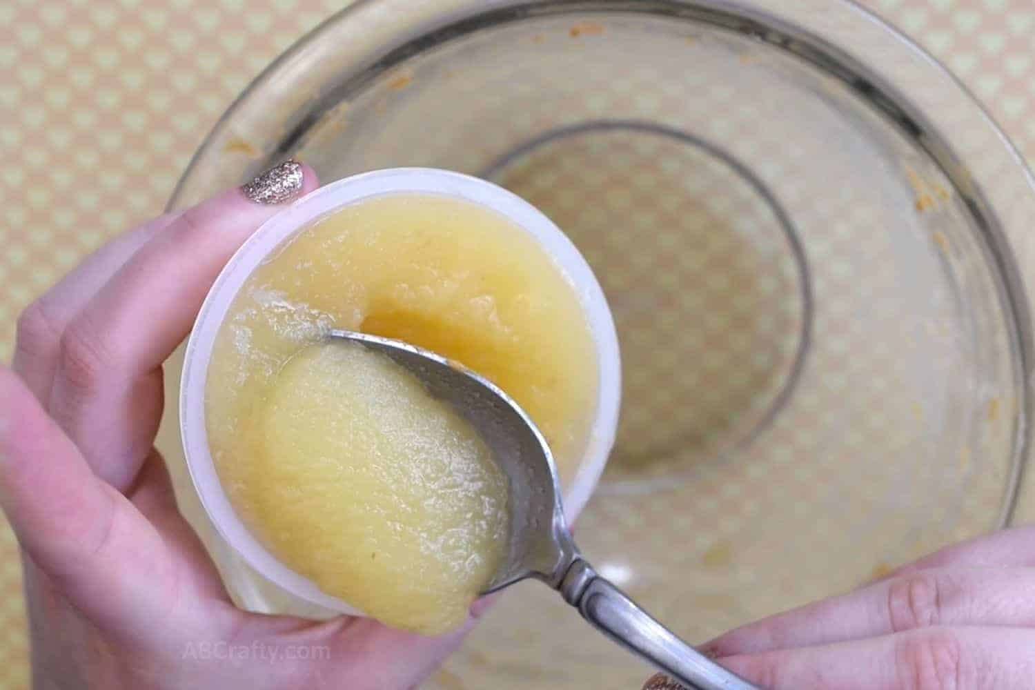 Scooping applesauce from a single serve applesauce container with a spoon over a bowl