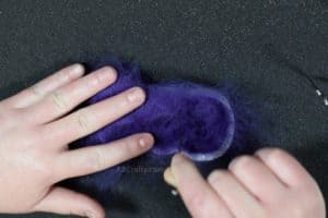 Needle felting purple wool over a catnip filled toy being made inside of a cookie cutter in the shape of a bunny