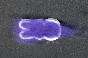 Purple wool placed on top of a cookie cutter in the shape of a marshmallow peep. The cookie cutter is on top of a black foam block
