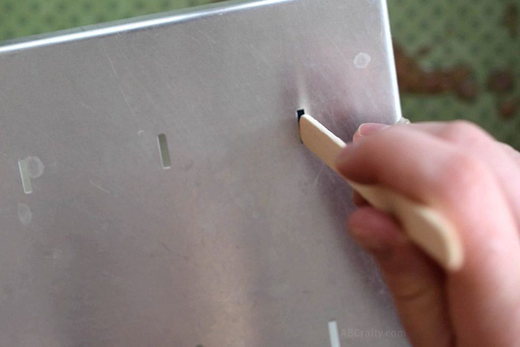 Inserting a popsicle stick into the metal top of a popsicle mold