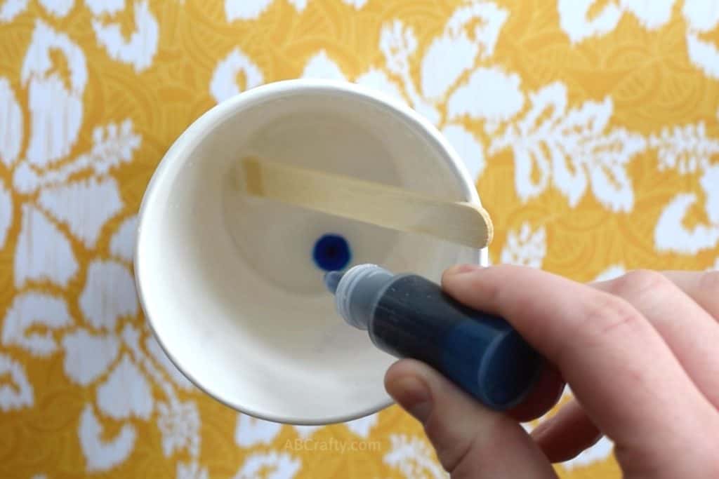 Squeezing blue soap dye into a paper cup that has melted clear glycerin soap