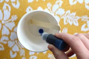 Squeezing blue soap dye into a paper cup that has melted clear glycerin soap