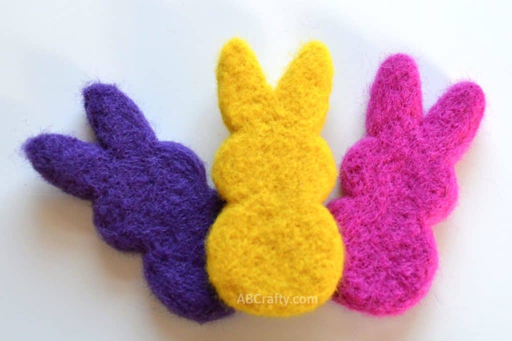 DIY catnip toys in the shape of marshmallow peeps in purple, yellow, and pink. All made of needle felted wool