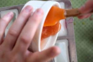Pouring orange glitter soap from a ramekin into mold