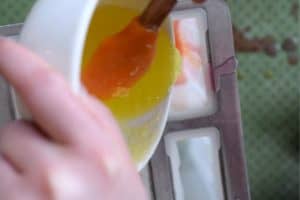 Pouring yellow glitter soap from a ramekin into mold