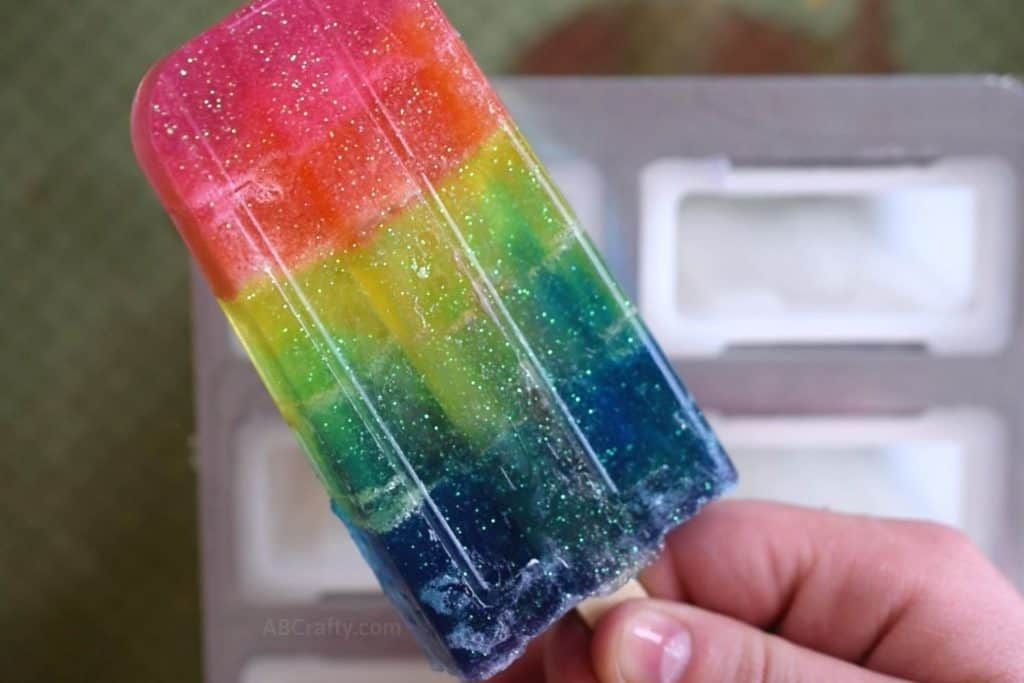 Holding a handmade glitter rainbow popsicle soap after removing it from the mold