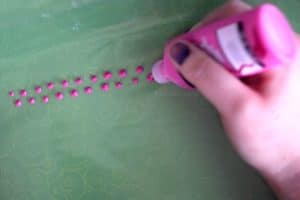 Painting two uneven rows of dots with pink fabric paint