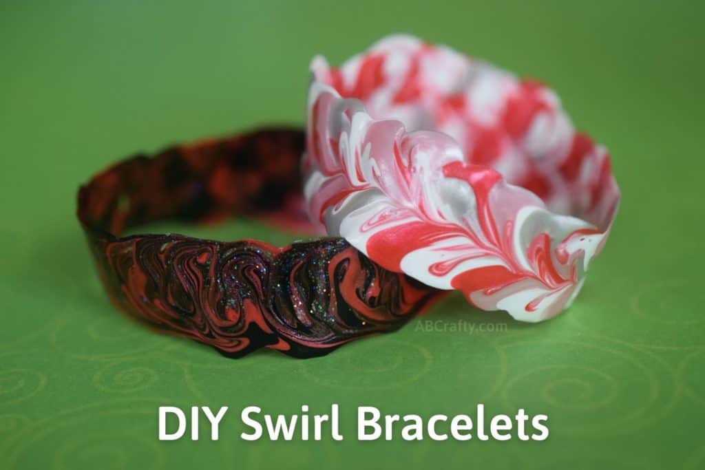 Two bracelets made of fabric paint. One is red, silver, and white, and the other is black and red with glitter. The text reads "DIY Swirl Bracelets"