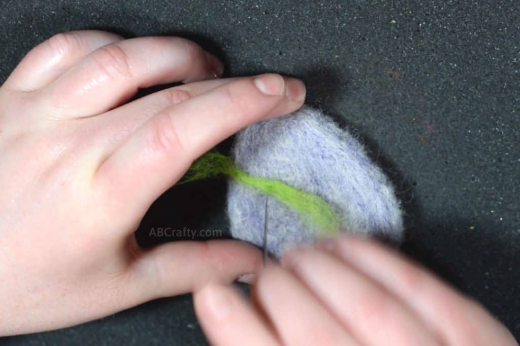 Needle felting a stripe of green wool onto a purple felted egg cat toy