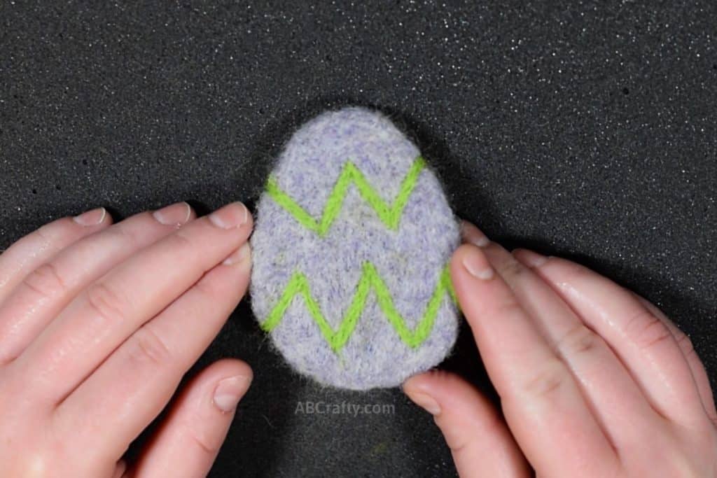 Holding finished felted purple Easter egg catnip toy with green zig zags across the egg, all made of wool