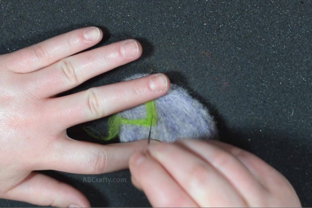 Needle felting a zig zag pattern with green wool onto a purple egg to make a felted Easter Egg