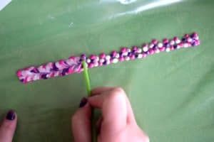 Using the back of a paintbrush to swirl purple, pink, and white fabric paint