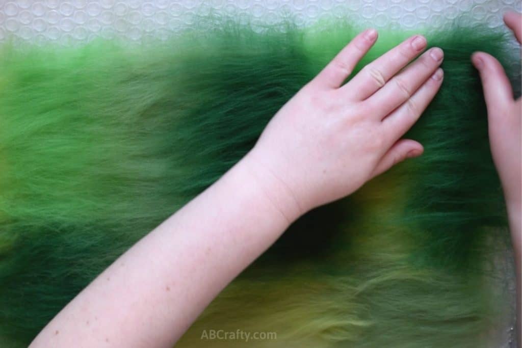 Placing green wool fiber in a rectangle over other green wool